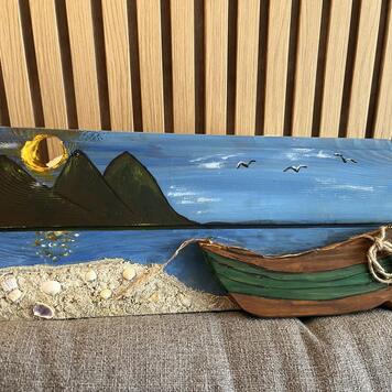 Handbemalte Holzdekoration — grünes Fischerboot am Sandstrand mit Muscheln, Berge und Möwen über der Bucht