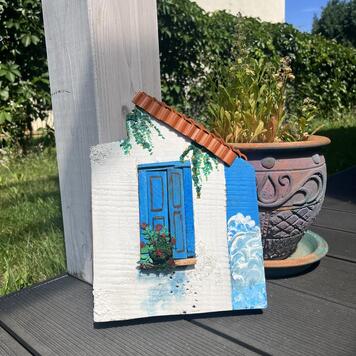 Handbemalte Holzdekoration — weißes Häuschen mit blauen Fensterläden, Terrakottadach und Blumen im griechischen Stil