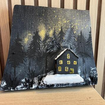 Décoration en bois peinte à la main — chalet sombre aux fenêtres éclairées dans une forêt enneigée sous des étoiles dorées