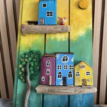 Décoration en bois peinte à la main — maisonnettes colorées sur des étagères en bois flotté, un arbre et un soleil sur fond jaune, vert et bleu