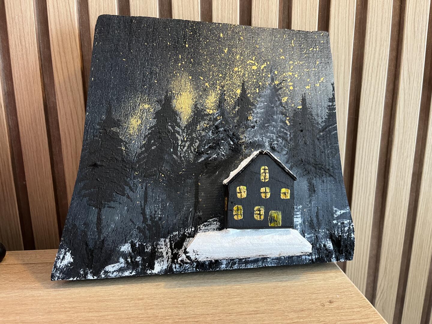 Handbemalte Holzdekoration — dunkle Hütte mit leuchtenden Fenstern im verschneiten Wald unter goldenen Sternen — Foto 1 / 4