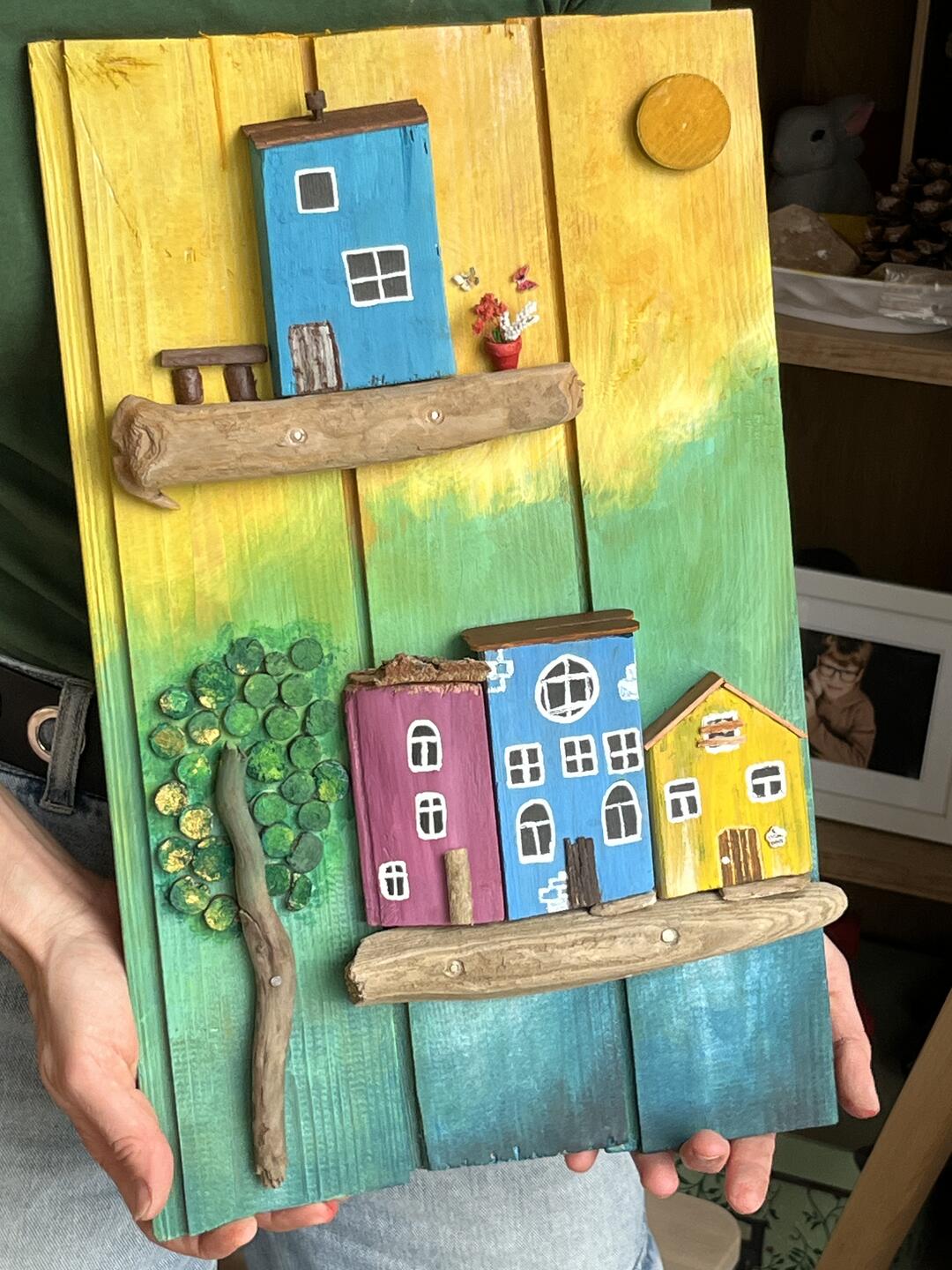Decorazione in legno dipinta a mano — casette colorate su mensole di legno di mare, un albero e un sole su sfondo giallo, verde e blu — foto 3 / 4